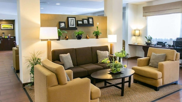A modern hotel lobby with a sofa set, two armchairs, a coffee table, and a reception desk.