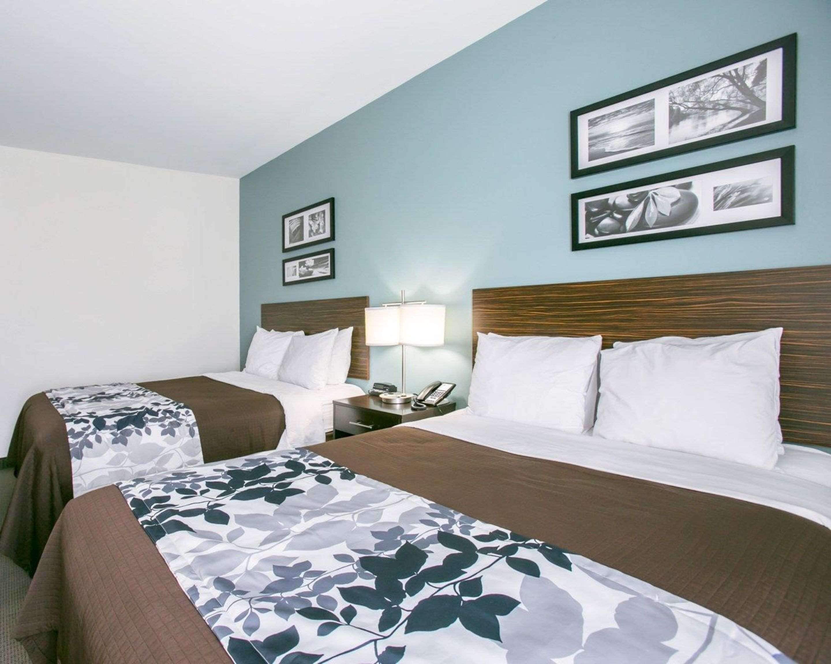 A hotel room with two beds, a nightstand with a lamp, and framed pictures on the wall.