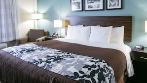 A hotel room with a large bed, two bedside tables, a chair, and a wall with three framed pictures.