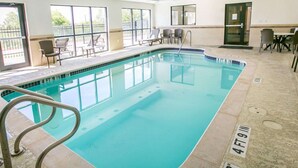 An indoor swimming pool with clear poolside chairs and a sunlit area with tables and chairs.