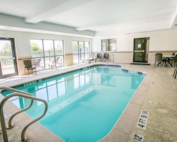 An indoor swimming pool with clear poolside chairs and a sunlit area with tables and chairs.