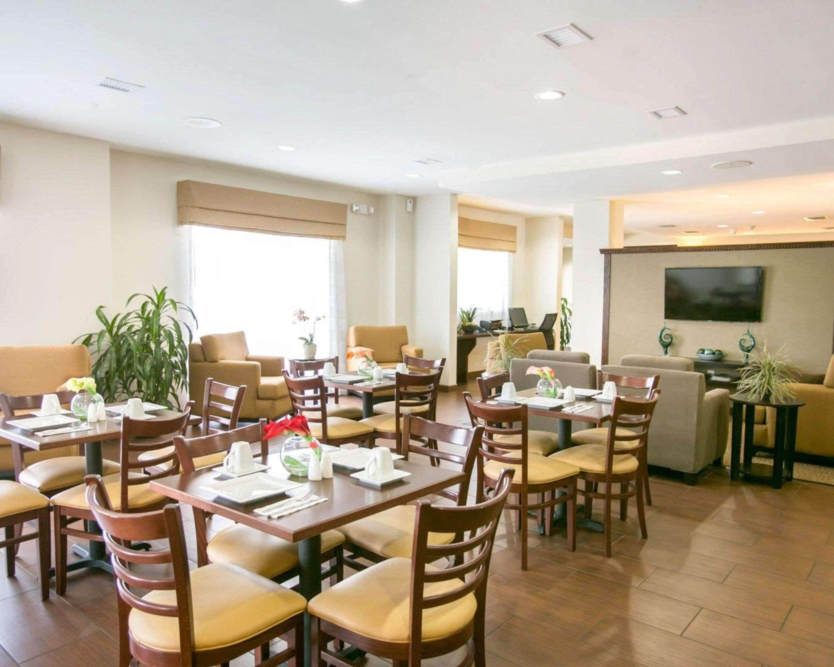 A hotel dining area with multiple tables and chairs, a sofa, and a television on the wall.