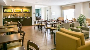A hotel lobby with multiple seating areas, including tables and chairs, and a reception desk with coffee and beverage dispensers.