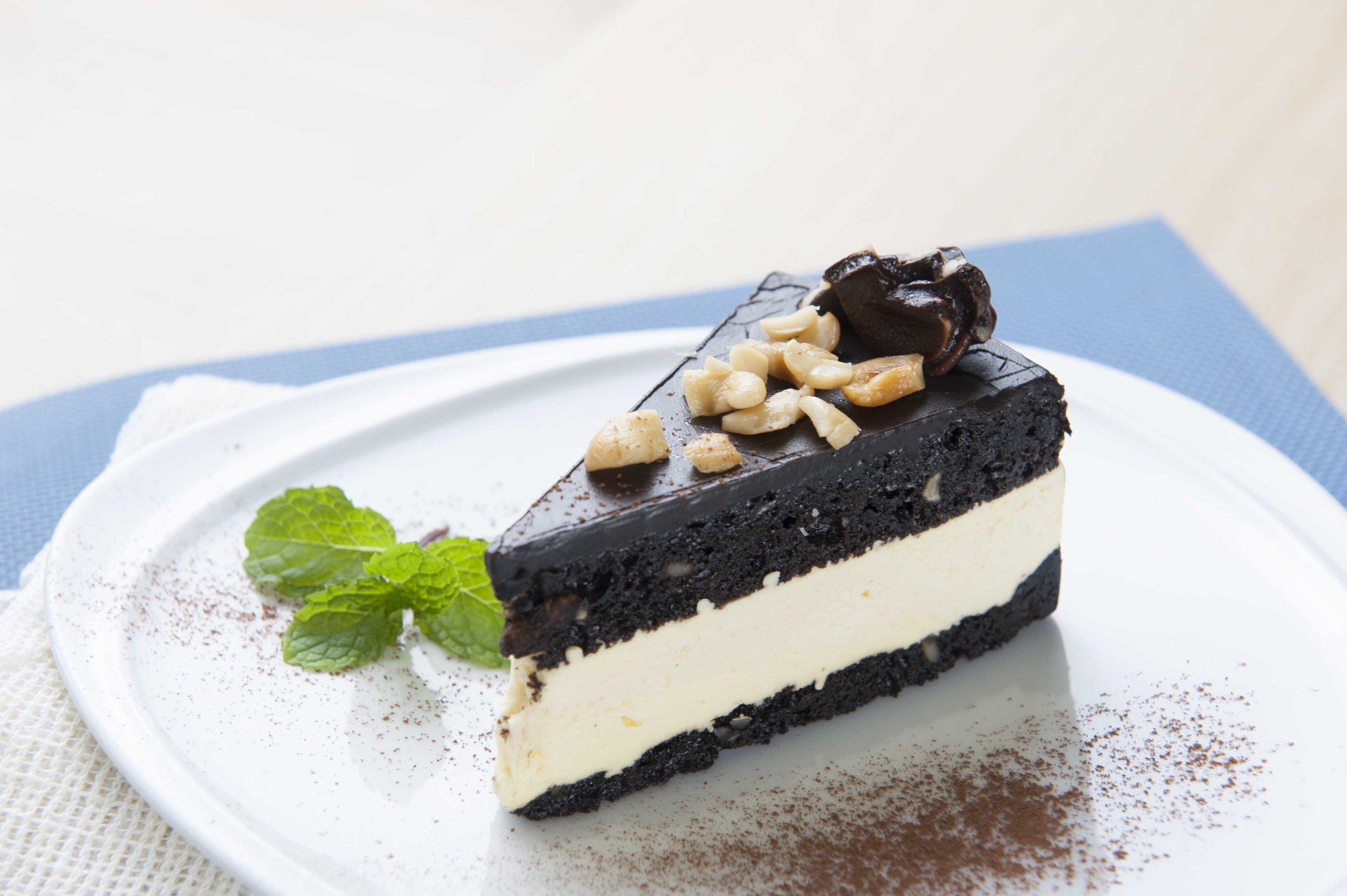 A slice of chocolate cake with a white cream layer and a mint leaf garnish on a white plate.