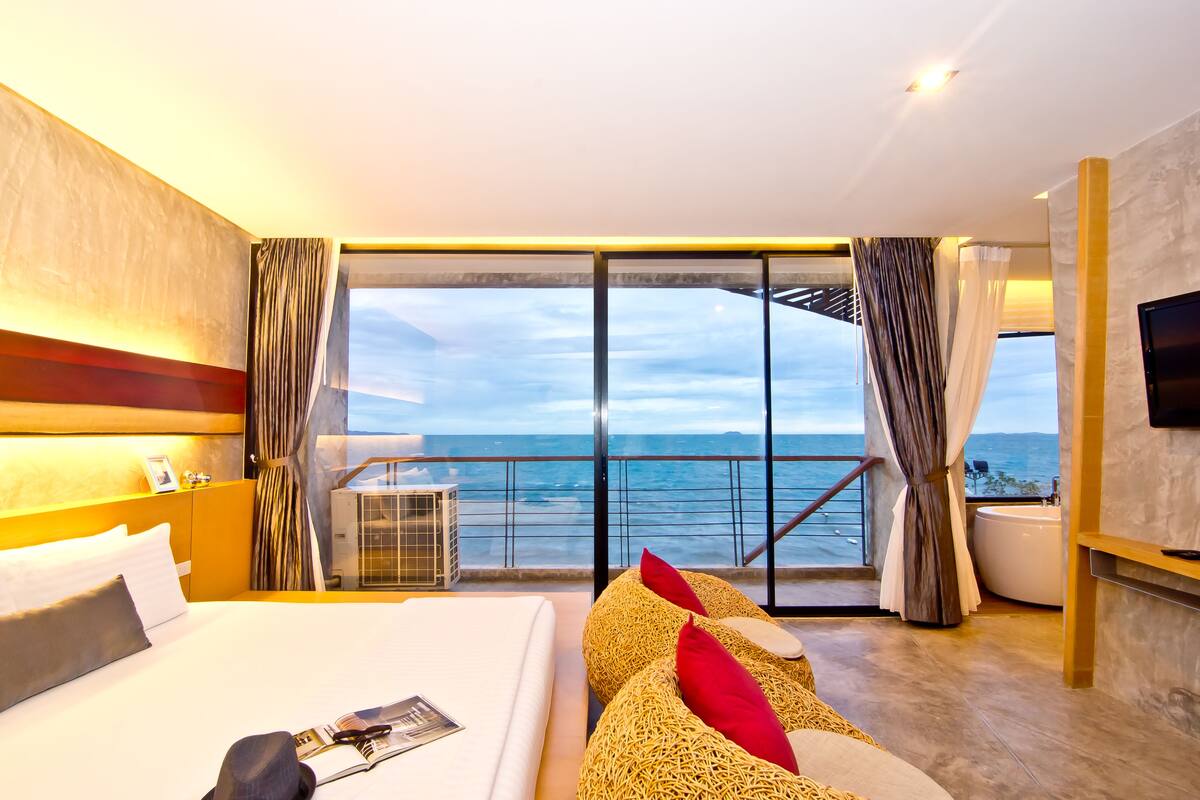A hotel room with a large bed, a view of the sea, a balcony, and a bathtub.