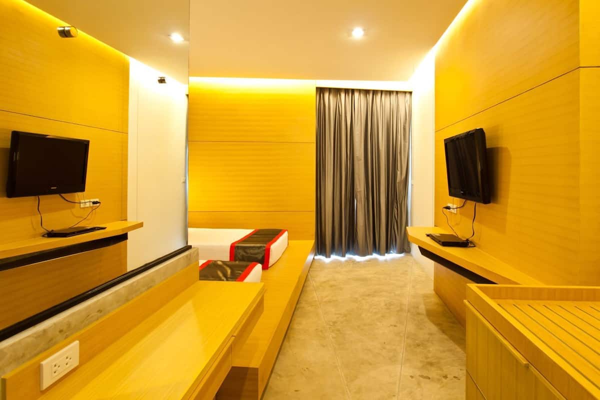 A modern hotel room with a bed, a TV, wooden furniture, and a curtain.