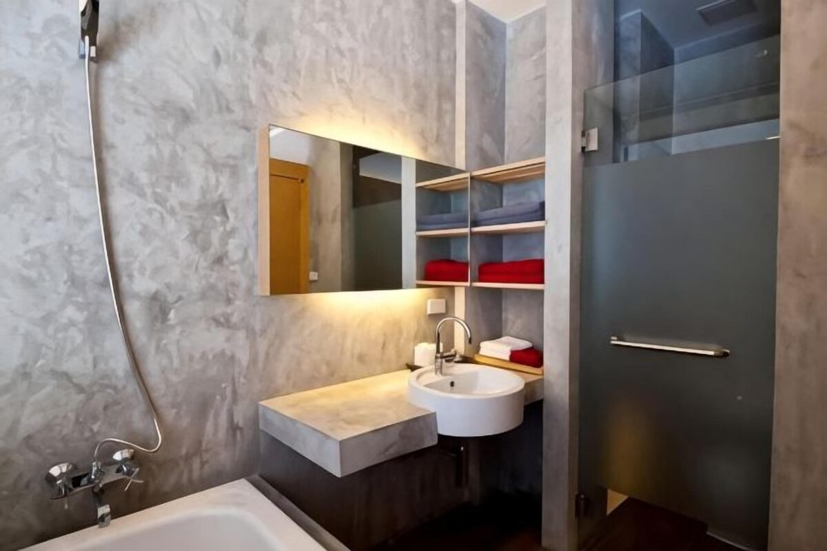 A modern bathroom with a marble wall, a white sink, a mirror, and a glass shower enclosure.
