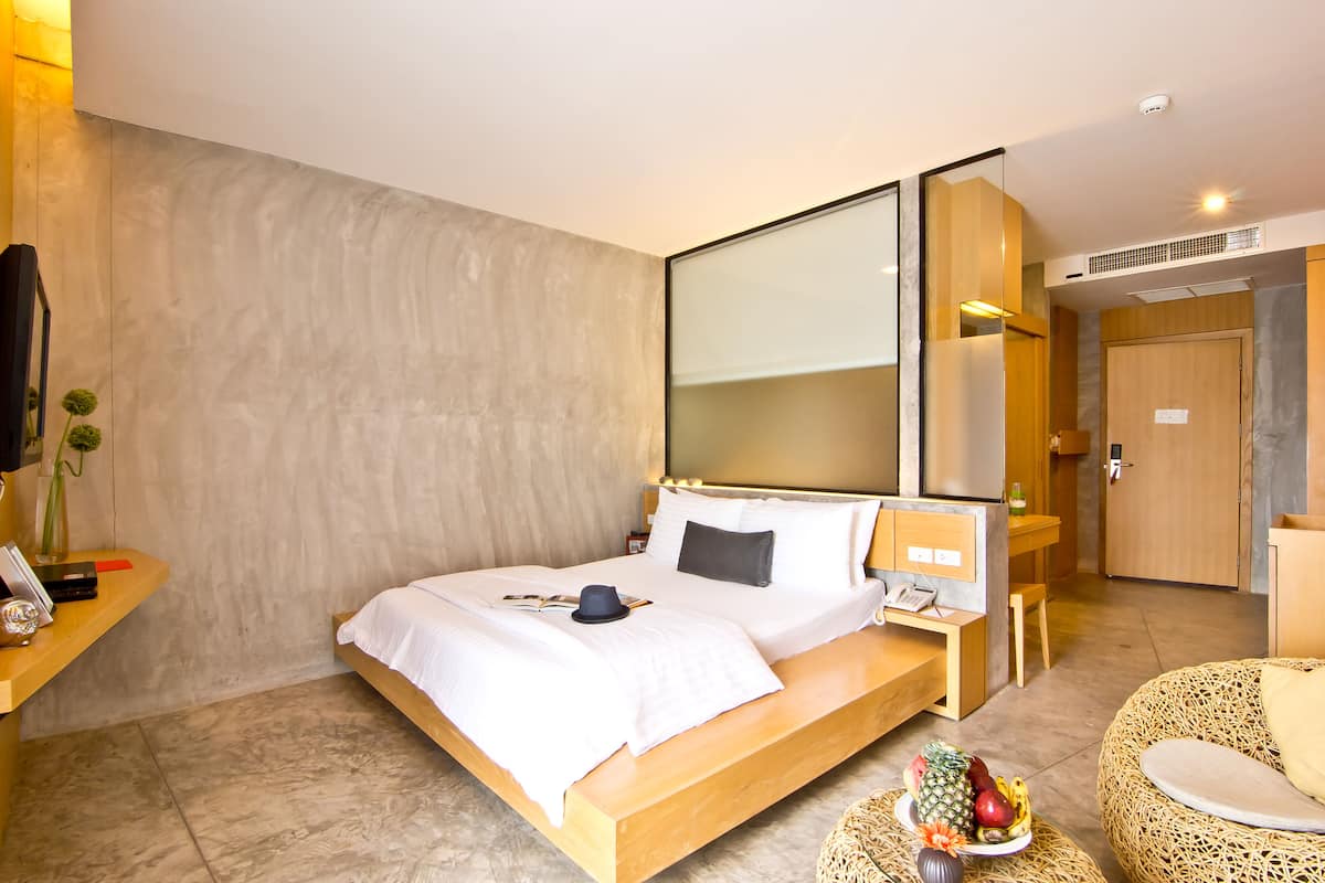 A modern hotel room with a large bed, bedside table, and a small round table with fruit.