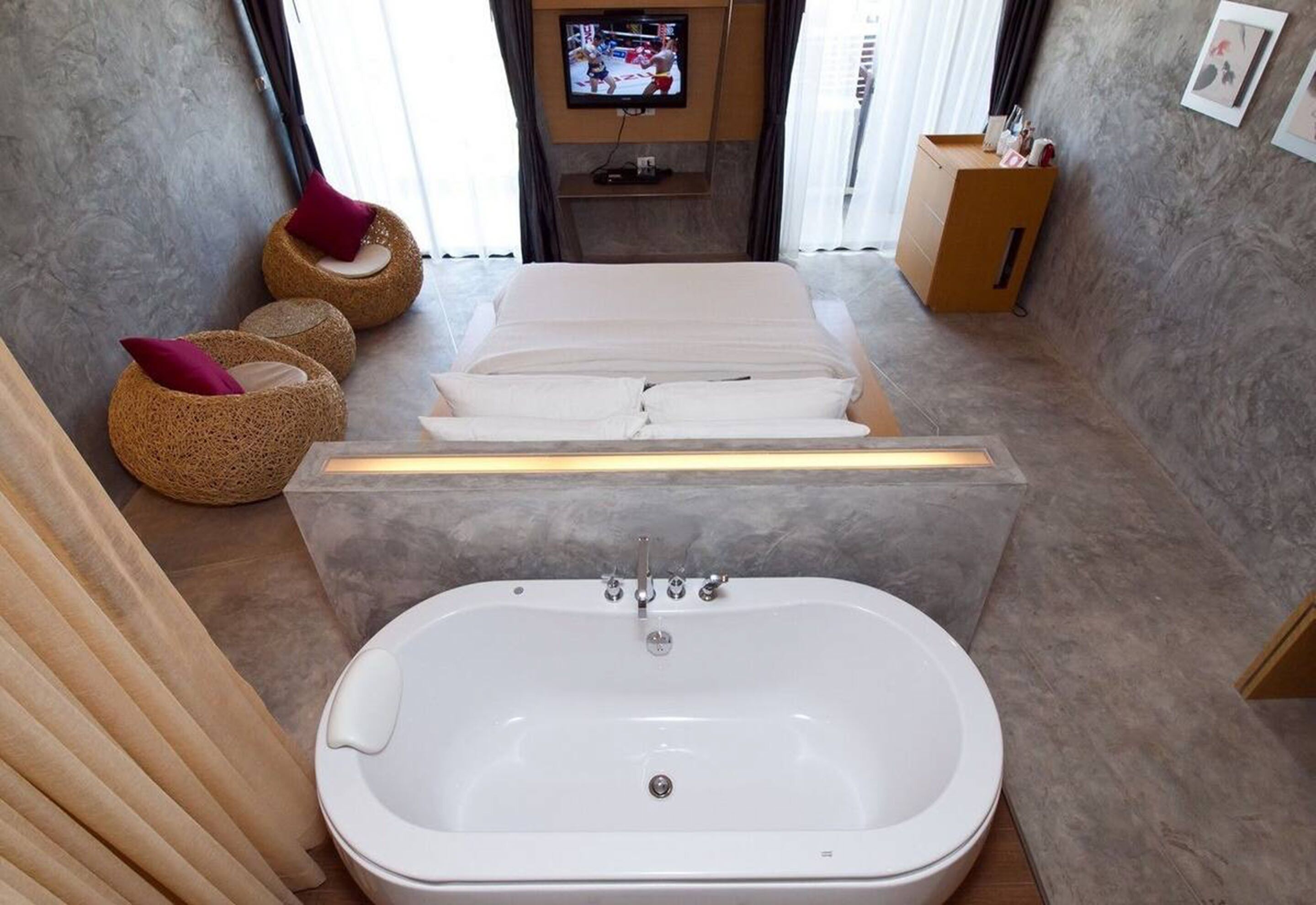 A modern bathroom with a large bathtub, a flat-screen TV mounted on the wall, and a wooden cabinet with toiletries.