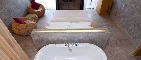 A modern bathroom with a large bathtub, a flat-screen TV mounted on the wall, and a wooden cabinet with toiletries.