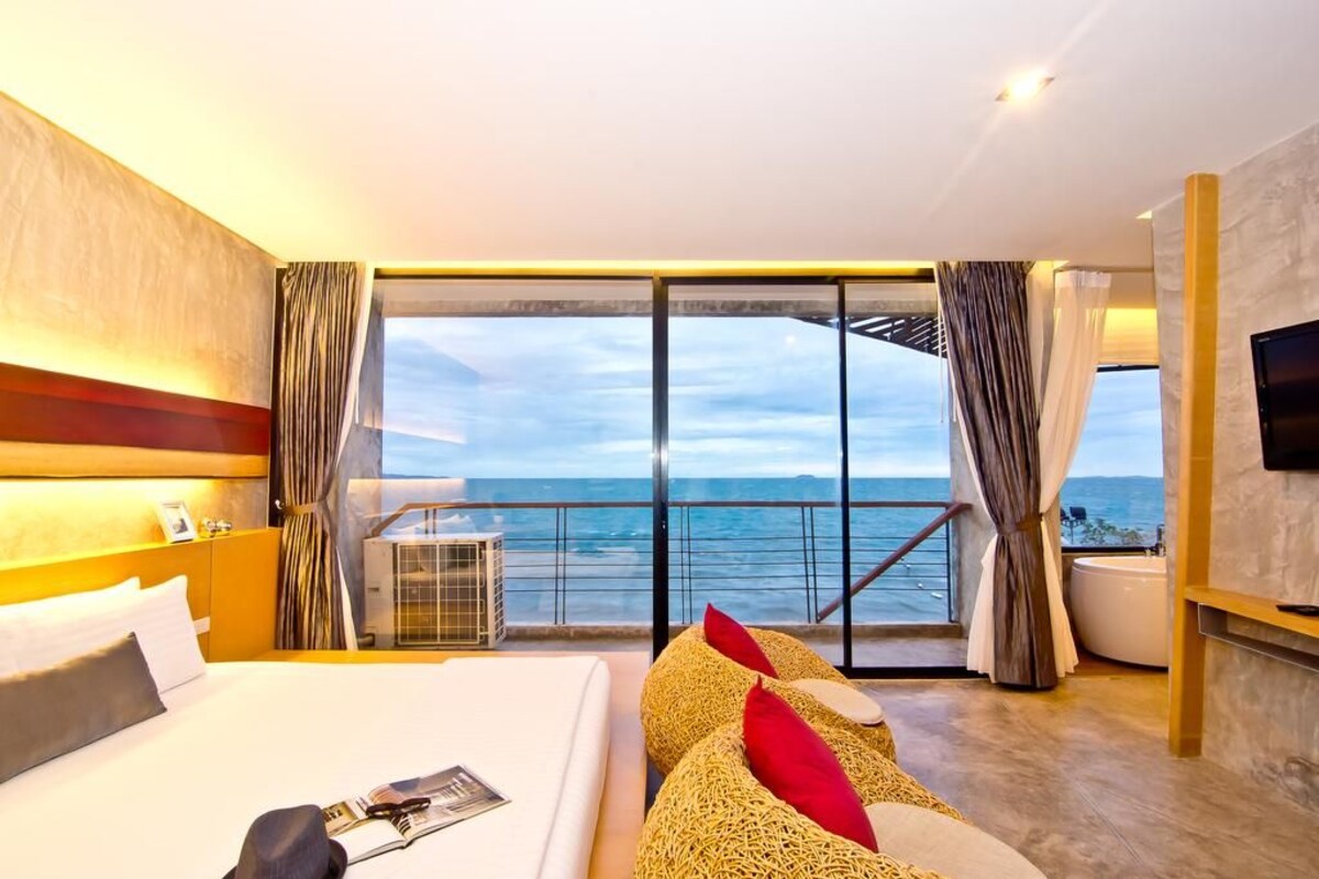 A hotel room with a large bed, a TV, a balcony with a view of the sea, and a bathtub.