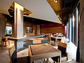 Un interno ristorante moderno con soffitti alti, condotti a vista e un mix di arredi in legno e metallo.