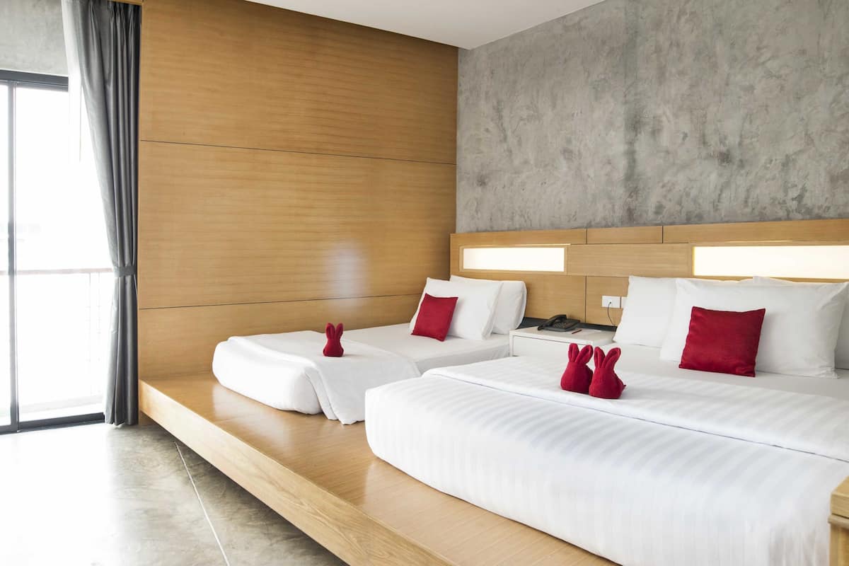 A hotel room with two beds, a wooden headboard, a concrete accent wall, and a large window with curtains.