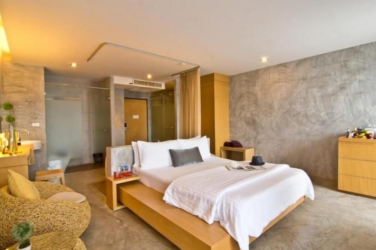 A modern bedroom with a large bed, bedside tables, a wooden dresser, and a walk-in closet.