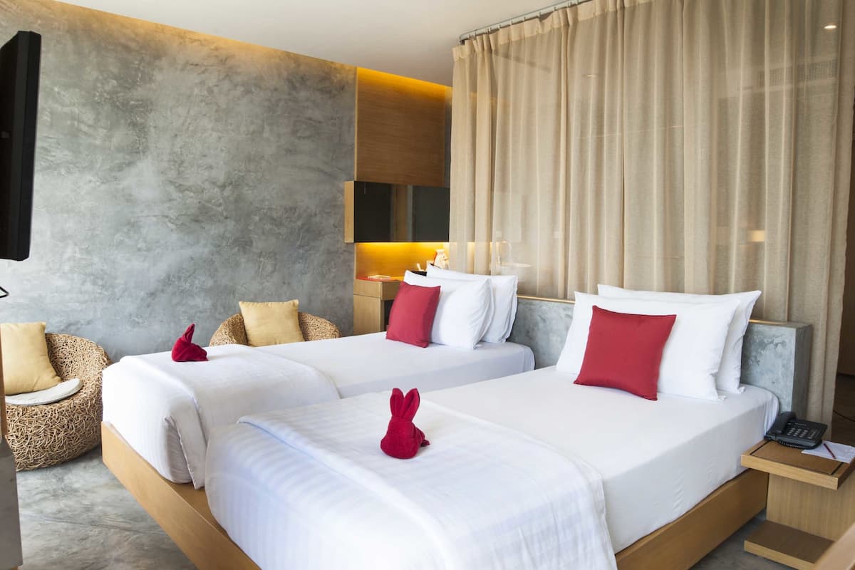 A hotel room with two beds, a sofa, a bedside table, and a bathroom area.