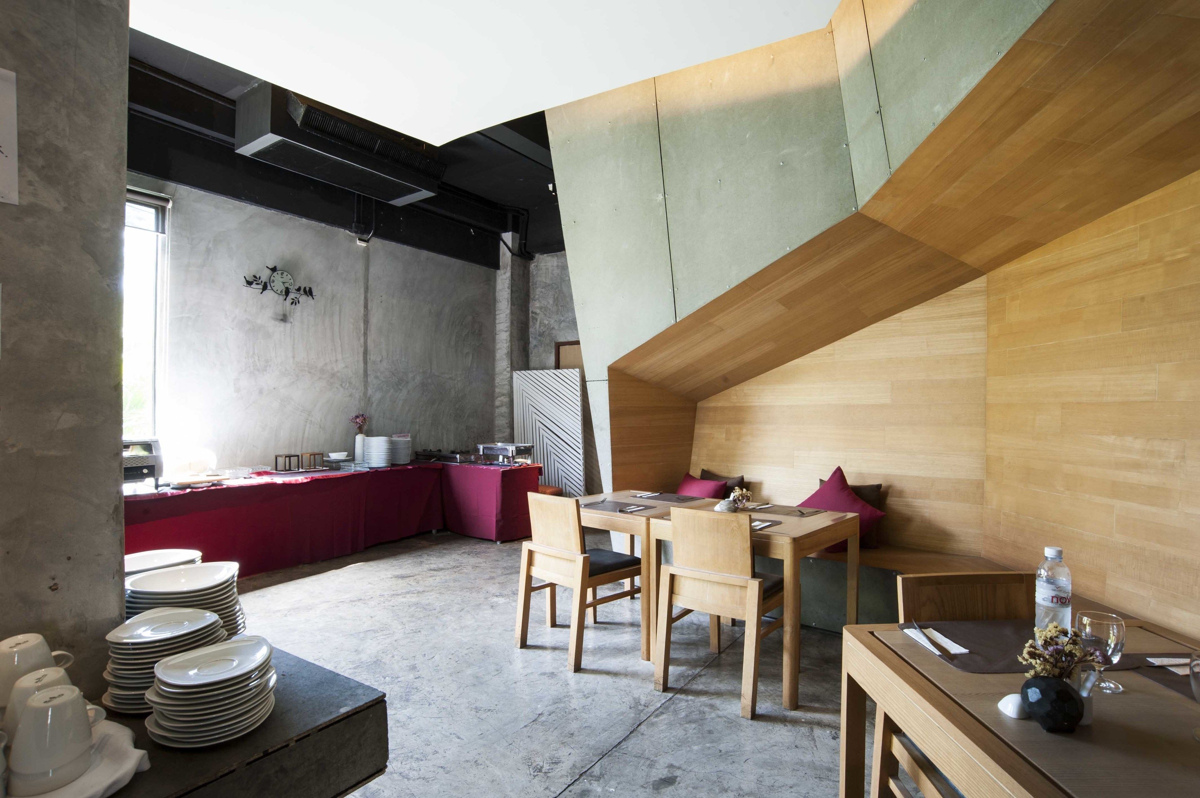 A modern dining area with a wooden table and chairs, a red buffet table, and a concrete wall with a clock.