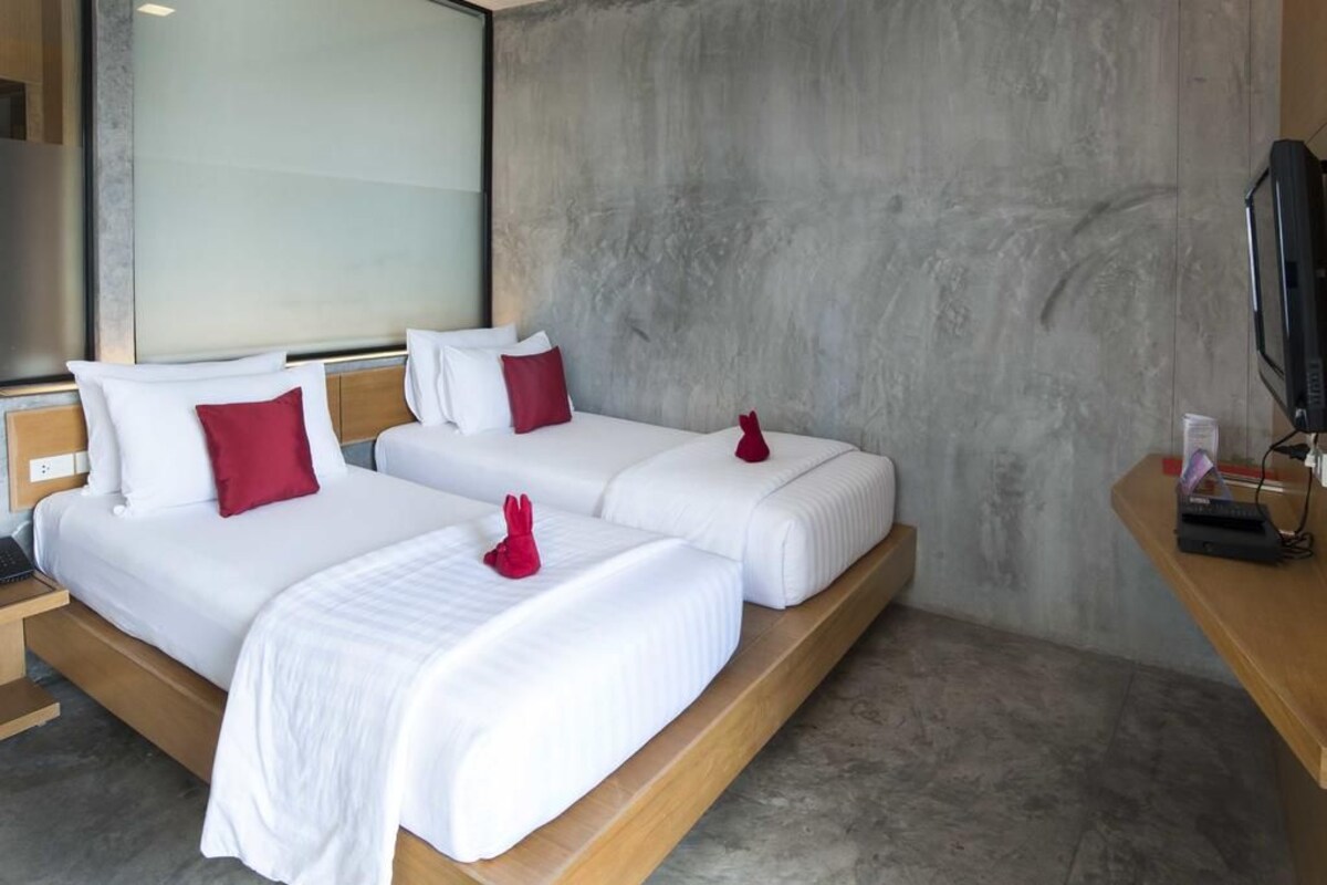A hotel room with two beds, each with white bedding and red pillows, a wooden headboard, and a large window.