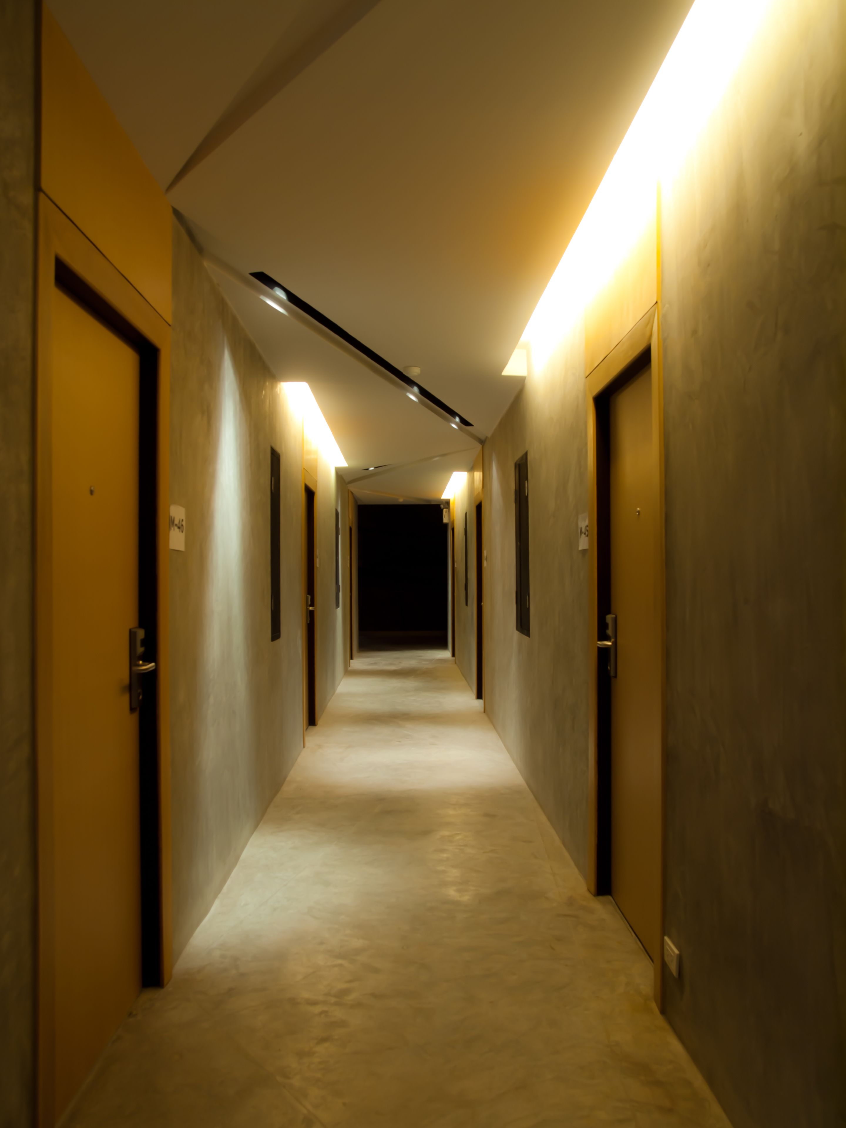 A hotel corridor with doors on both sides, a carpeted floor, and overhead lighting.