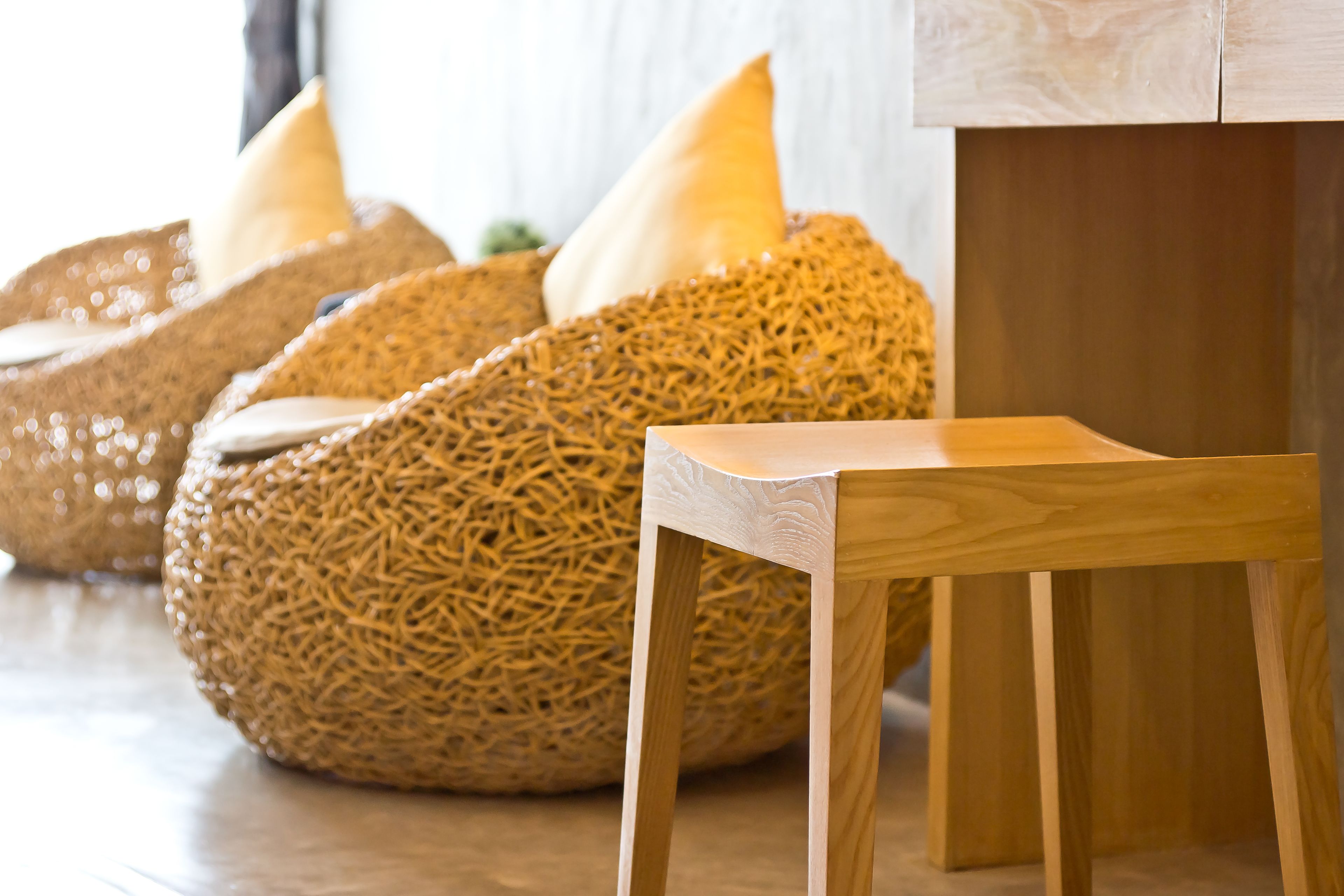 A wooden chair and woven poufs with cushions in a room.