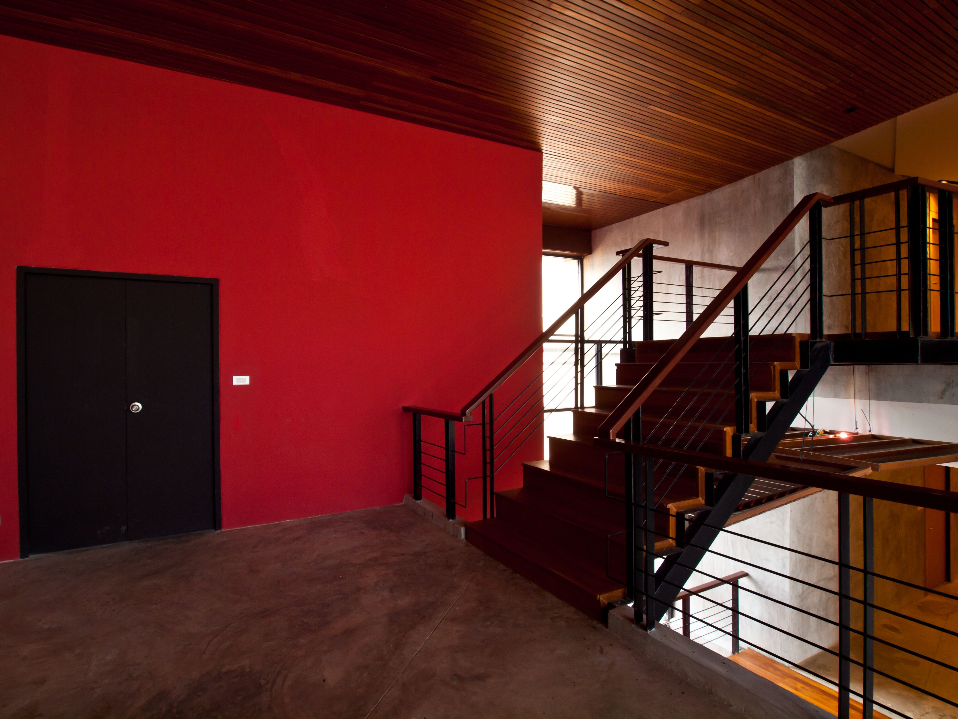 A modern interior with a red wall, a wooden staircase, and a black door.