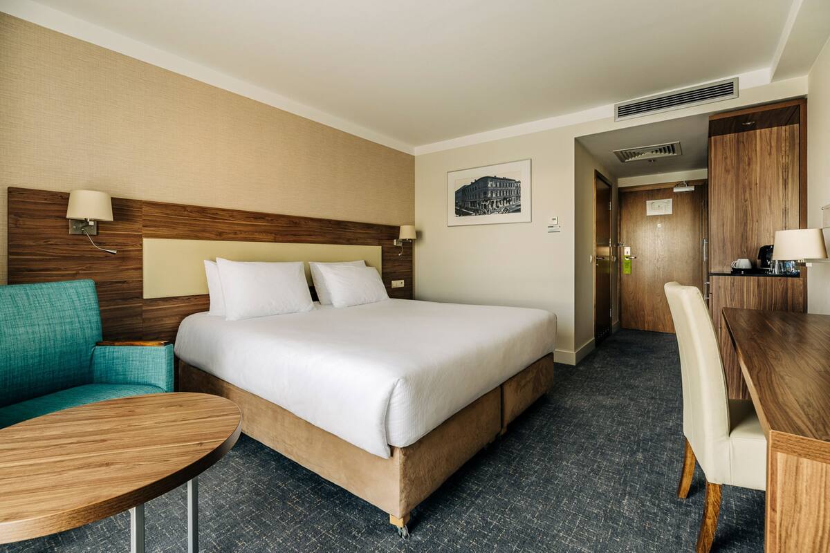 Una habitación de hotel con una cama grande, un área de descanso con una mesa, un sofá y una puerta que da a un baño.