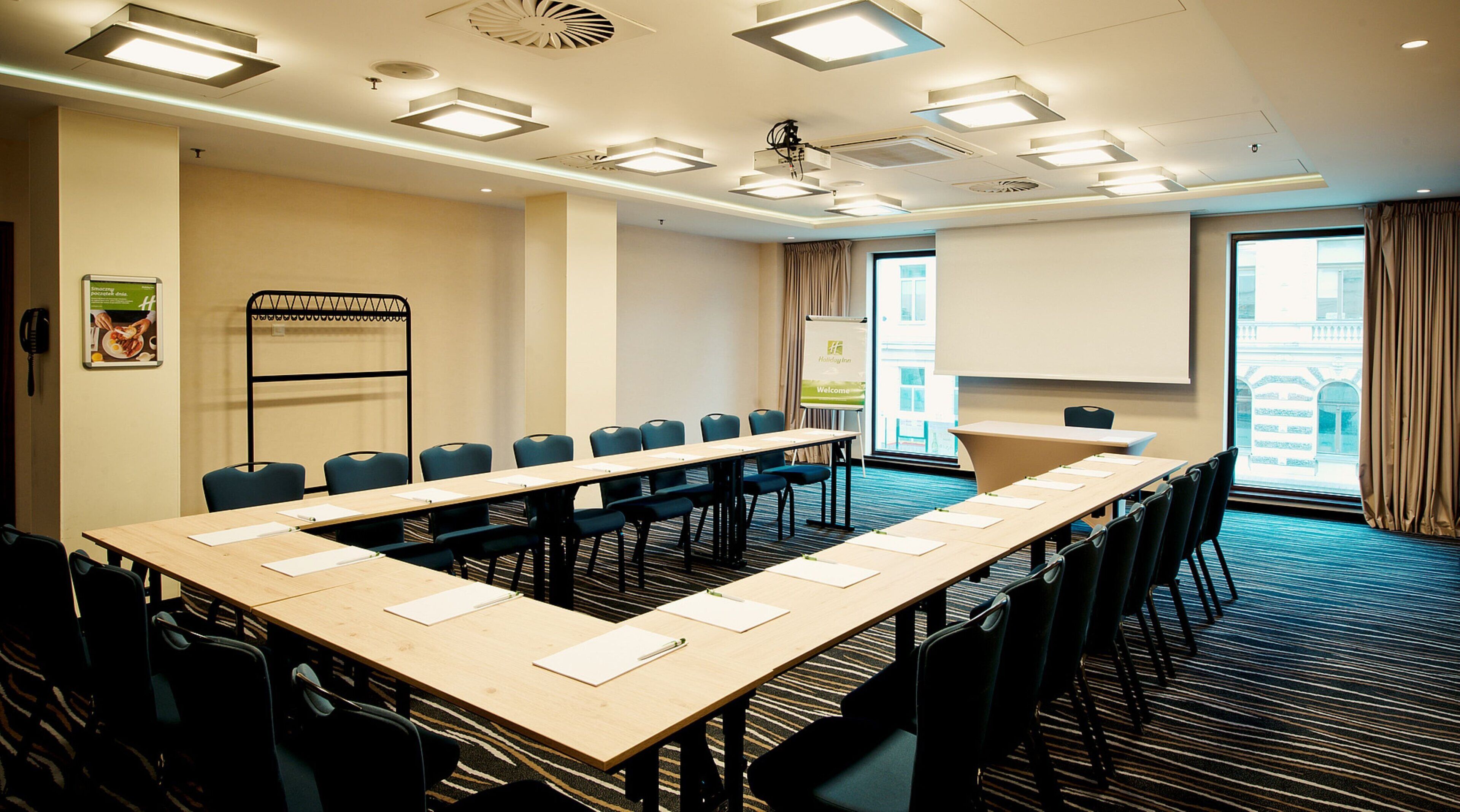 A conference room with a long table, multiple chairs, a projector screen, and a whiteboard.