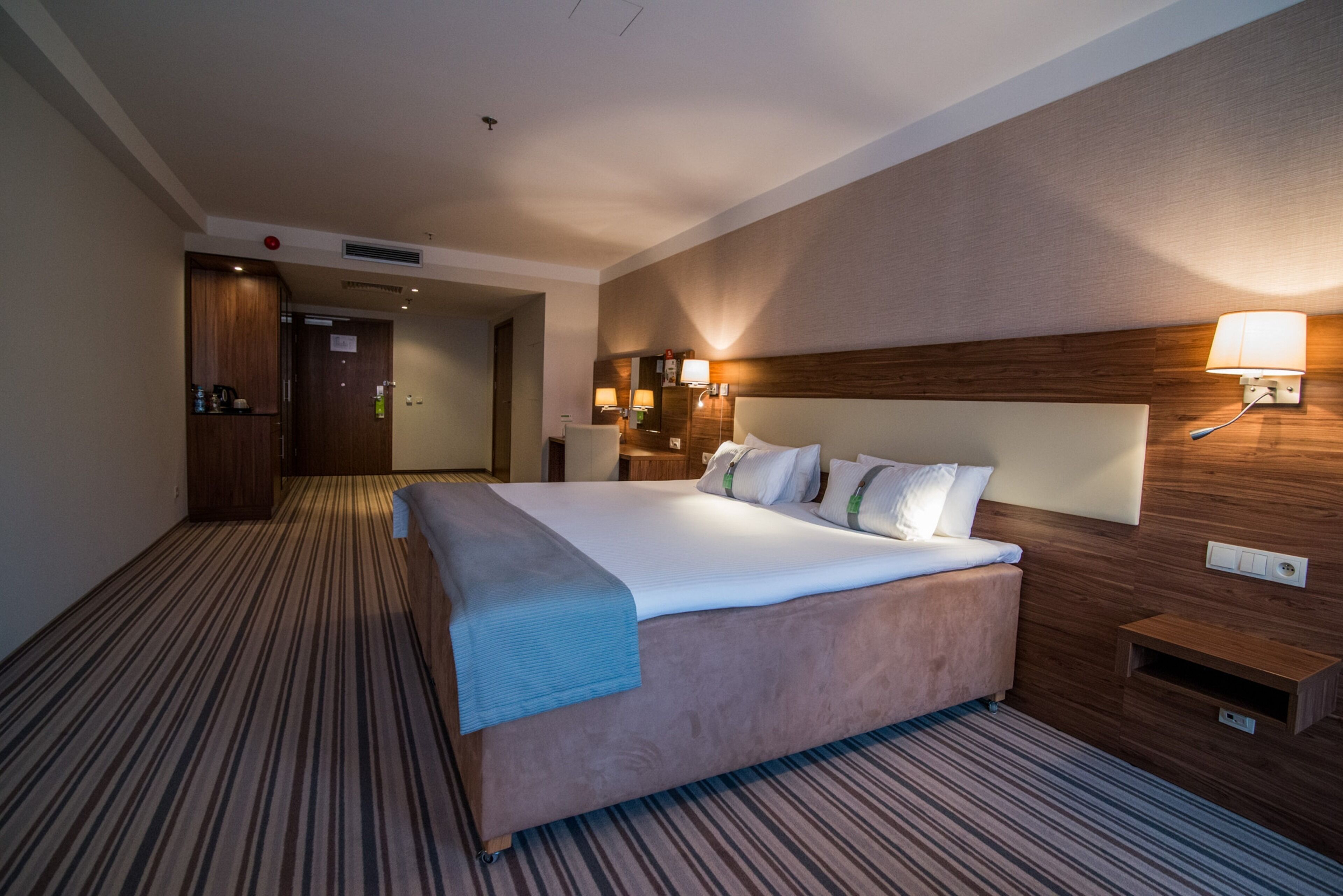 A hotel room with a large bed, wooden headboard, and two bedside lamps.