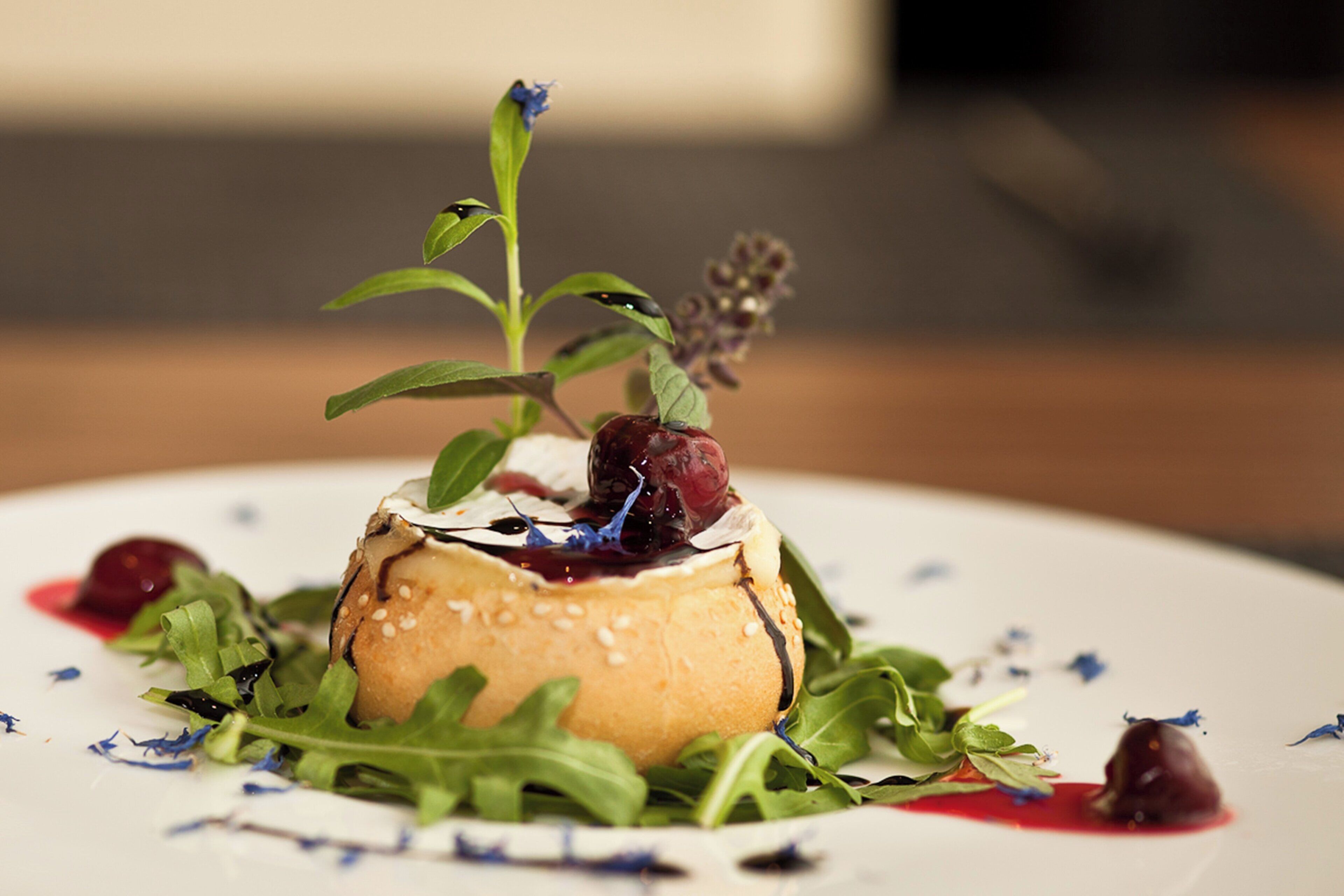 Un dessert dont la base est sphérique, surmonté d’une feuille, de baies et d’une petite plante.