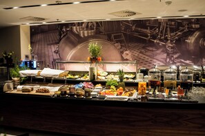 Buffet com diversos alimentos e bebidas, incluindo frutas, doces e acompanhamentos.