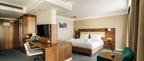 A hotel room with a wooden desk, a bed, a TV, and a green chair.