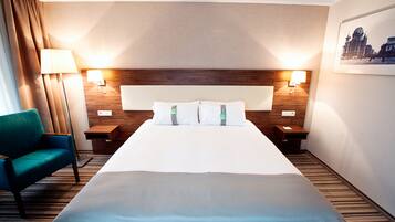 Habitació d'hotel amb un llit gran, dues taules de nit, una petita taula auxiliar, una cadira i una làmpada penjada a la paret.