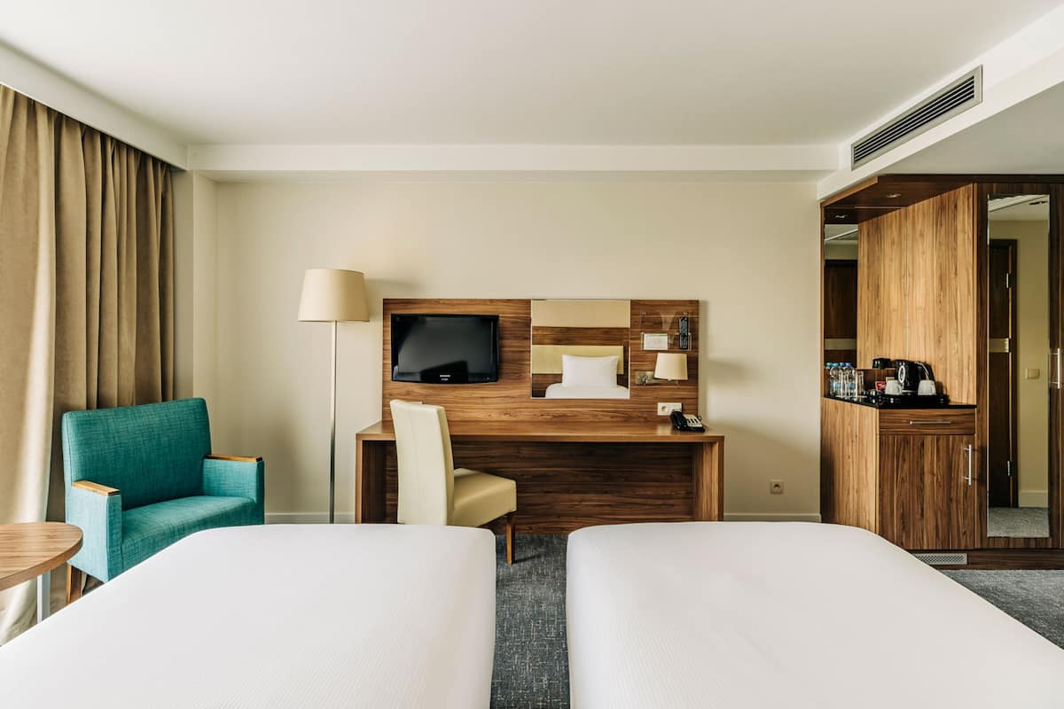 Una habitación de hotel con dos camas, un escritorio, un televisor, una silla y un armario.