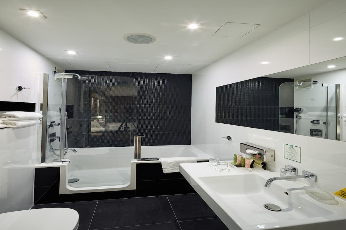 Un baño moderno con cabina de ducha de vidrio, bañera, lavabo doble e inodoro.