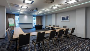 A conference room with a long table, chairs, a projector screen, and a "Welcome" sign.