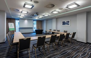 Uma sala de conferências com uma mesa comprida, cadeiras, uma tela de projetor e uma placa com a palavra 'Welcome'.