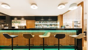 A bar area with a wooden counter, bar stools, and a shelf with bottles.