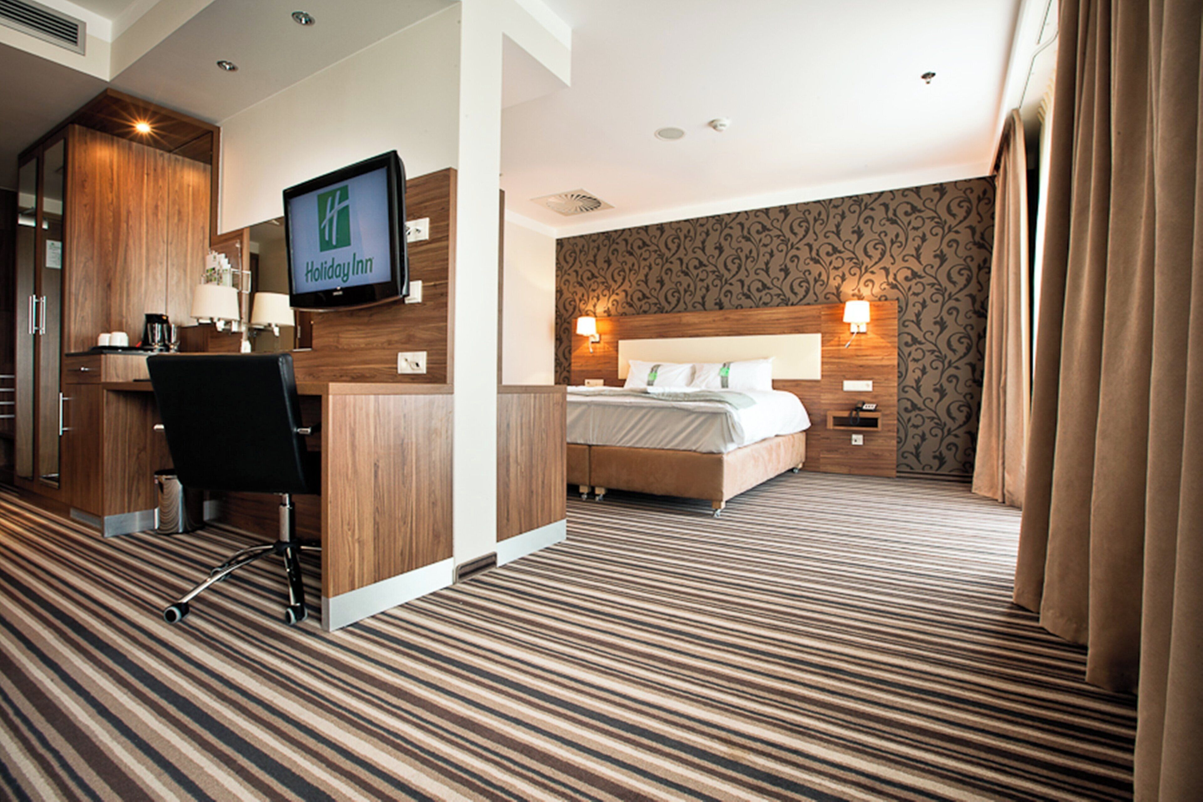 A hotel room with a bed, a desk, a chair, a television, and a patterned wall.