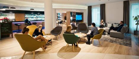 Un hall de hotel con zona de bar, asientos y una pantalla de televisión.