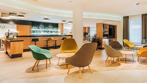 A modern hotel lobby with a bar area, seating arrangements, and a large window with curtains.