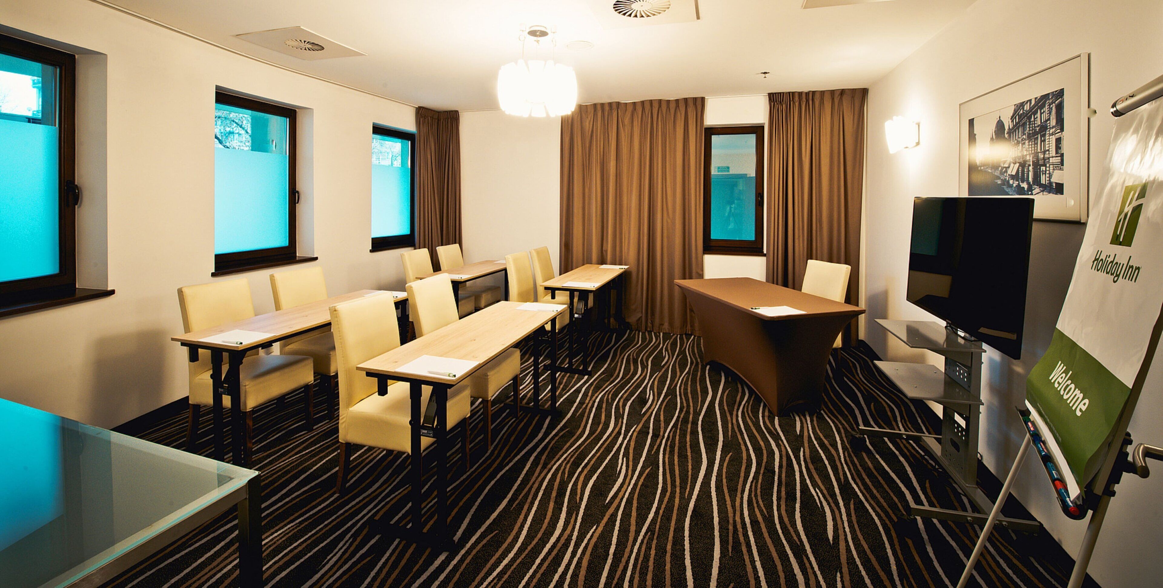 A hotel room with a conference table, chairs, a television, and a patterned carpet.