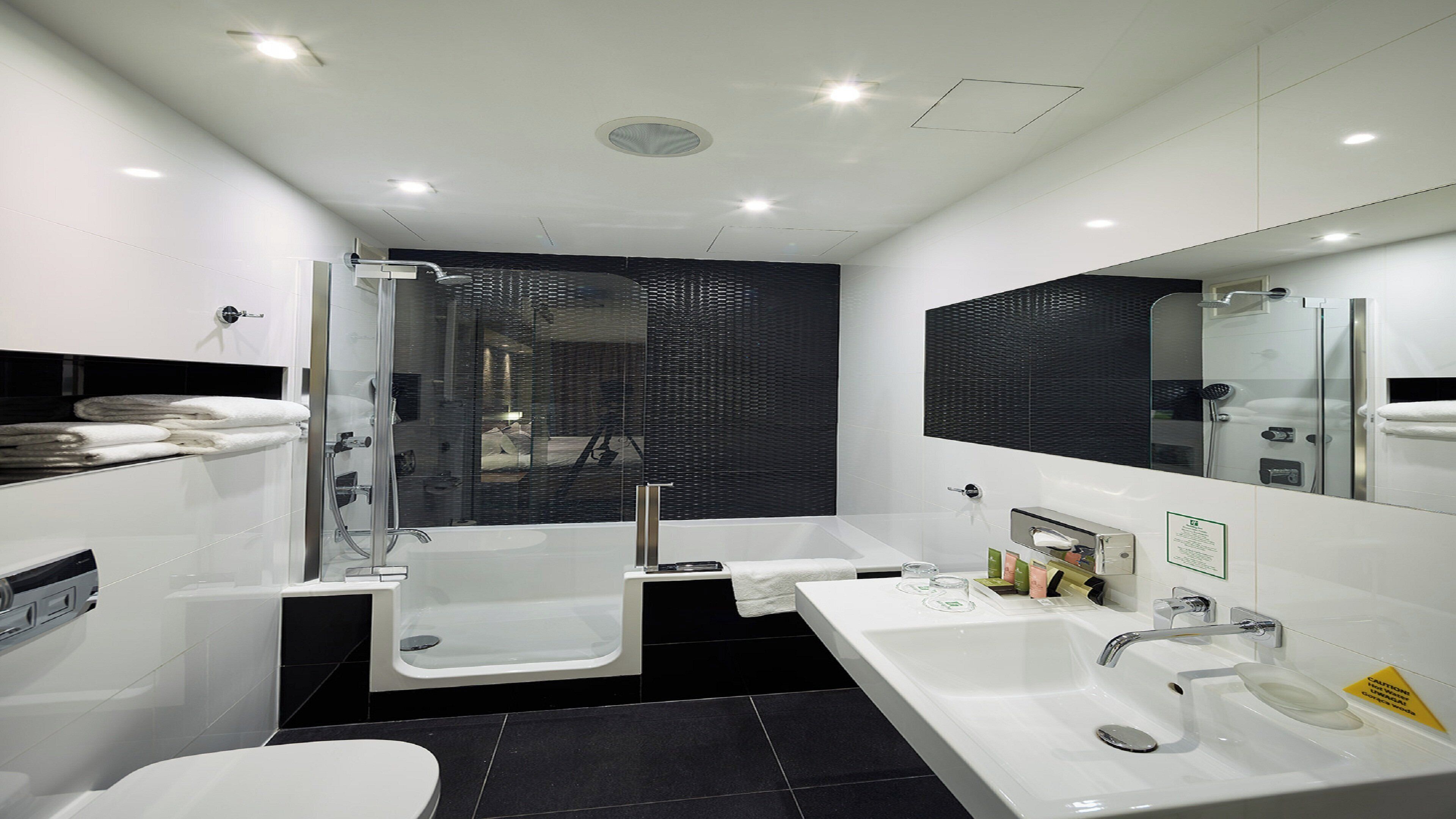 Un baño moderno con ducha, dos lavamanos, inodoro y un espejo grande.