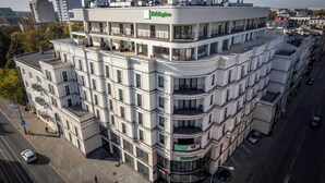 A multi-story hotel with a modern design, featuring balconies on each floor, a prominent 'Holiday Inn' sign, and a corner location with a street view. - Holiday Inn Lodz by IHG (Lodz)