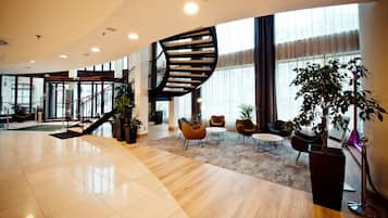 Un vestíbulo amplio con una escalera curva, zona de estar y ventanas grandes.