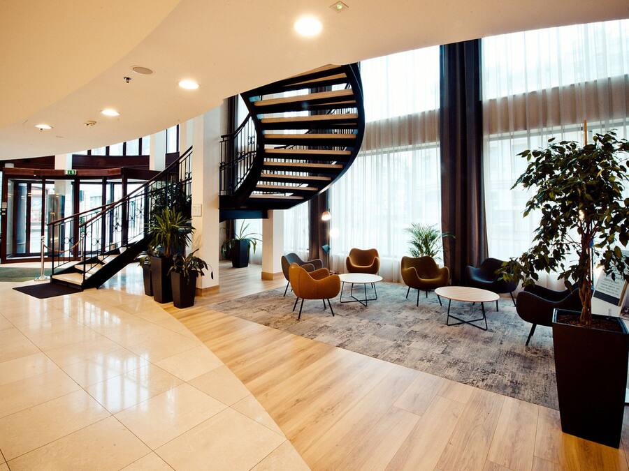 Un vestíbulo amplio con una escalera curva, zona de estar y ventanas grandes.
