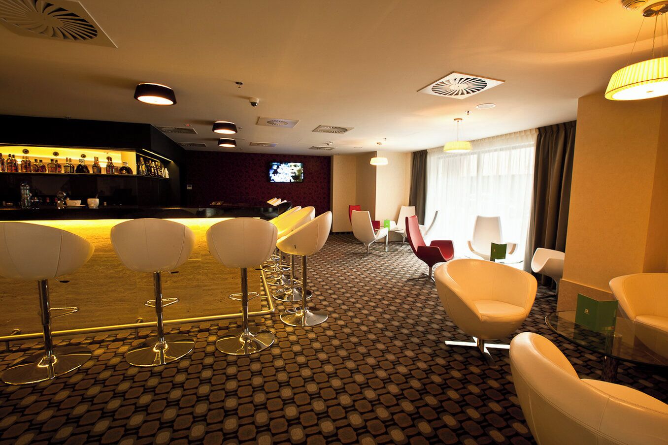 A hotel lobby with a bar area, seating arrangement, and a television screen.