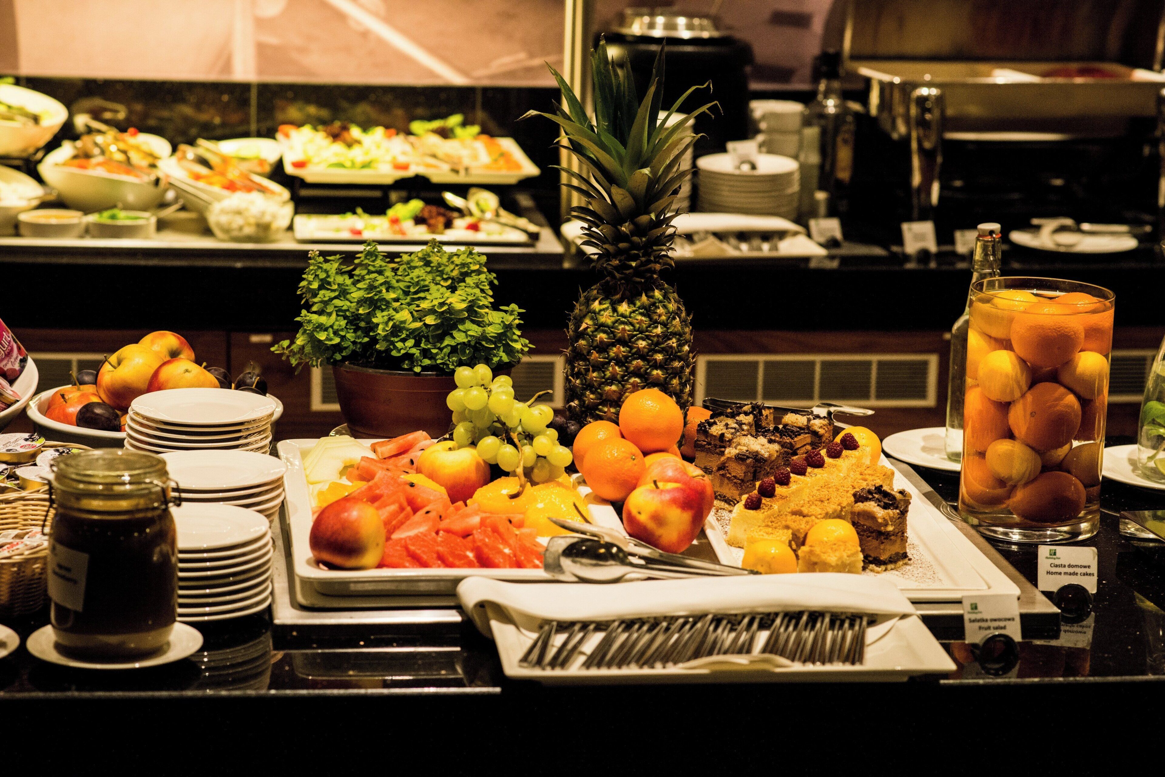 Un buffet proposant une variété de fruits, un ananas et un verre de jus d’orange.