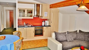 Un espacio habitable compacto con kitchenette, comedor y zona de estar con sofá y mesa de centro.