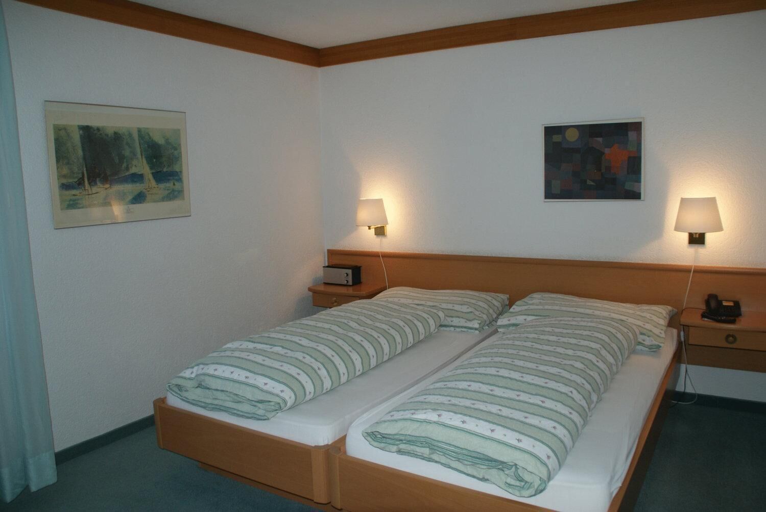 A double bed with two bedside tables, each with a lamp, in a hotel room with plain walls and a painting above the bed.