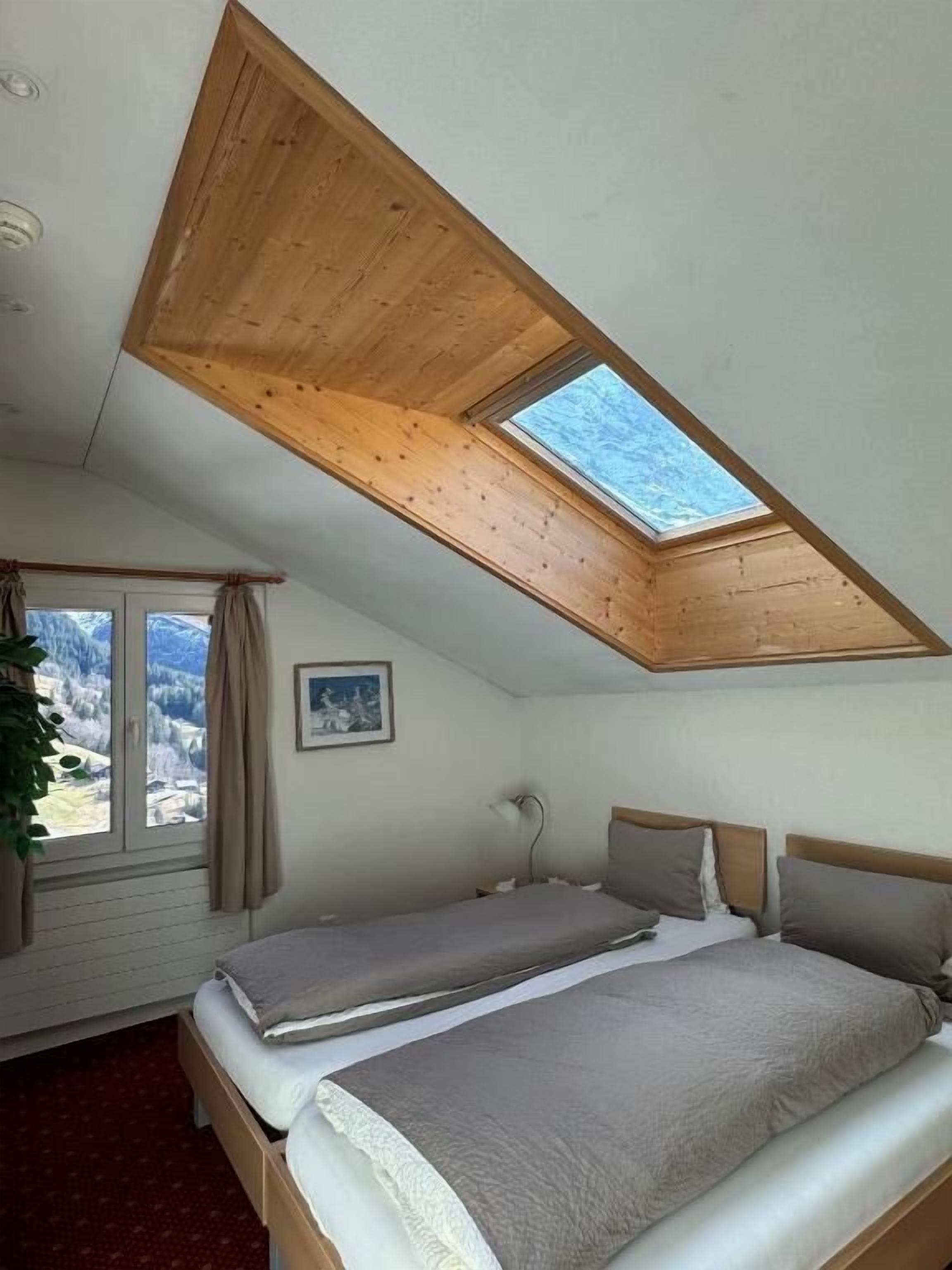 Un dormitorio con techo inclinado, dos camas, un ventanal con cortinas y vistas al exterior.
