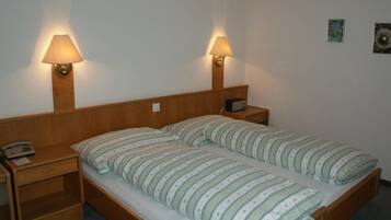 Een eenpersoonsbed met gestreept beddengoed, twee bedlampen, een bedtafeltelefoon en een klein tafeltje met een radio.